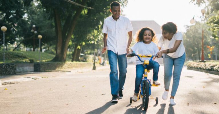 Parks - Man Standing Beside His Wife Teaching Their Child How to Ride Bicycle